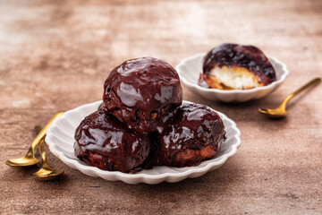 Chocolate Profiterole on a brown background, cream puff, or chou à la crème is a filled French choux pastry ball with  filling of whipped cream, garnished with chocolate sauce.