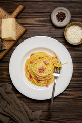 Pasta carbonara, spaghetti, pancetta, egg yolk and parmesan cheese, black pepper on a wooden background. Top view. Vertical image.