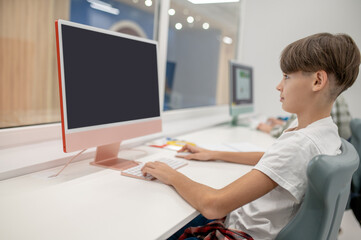 A schoolboy sitting at the computer at school and looking involved