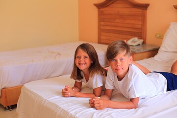 Two children lie on a bed with white sheets in a hotel room on vacation. Children play on the bed with white sheets at home. Boy and girl before going to bed at home