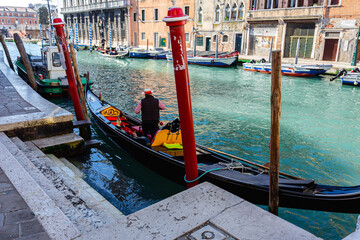 Venetian gondolier punting gondola on green canal waters of Venice Italy