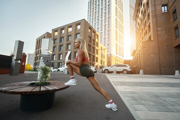 fit and young woman doing stretching in the city. A young fitness runner stretches her legs before a run. sports at dawn