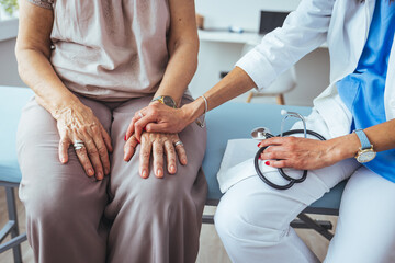 Doctor and patient are discussing something in clinic, just hands at the desk. Medicine and best service concept. Doctor woman encourage senior woman patient by holding hand.