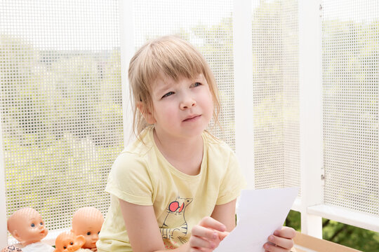 Calm Curious Elementary School Age Girl Sitting On A Balcony, Portrait, Squinting Eyes Face Closeup, One Person, Real People Lifestyle, Natural Portrait, Bright Outdoors Shot, Childhood Concept