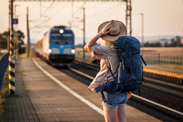 Travel by train. Woman backpacker standing at railroad station - obrazy, fototapety, plakaty