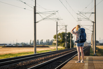 Woman traveler with backpack waiting for train at railway station