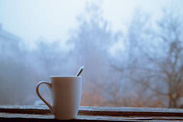 Soft focus foggy morning  scenery from the window . Autumn dawn with hot drink cup.  Cold season...