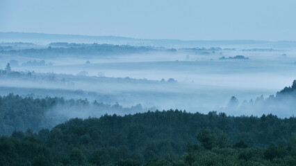 The landscape is foggy in a hilly area covered with forests in the morning without bright sunlight and without people