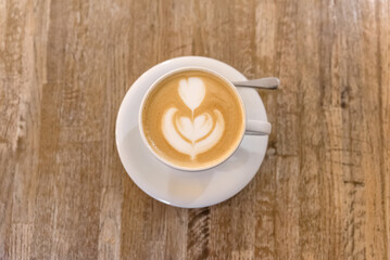 Cappuccino coffe in white cup with latte art on wooden table