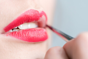 Closeup of girl paints lips with bright red lipstick.