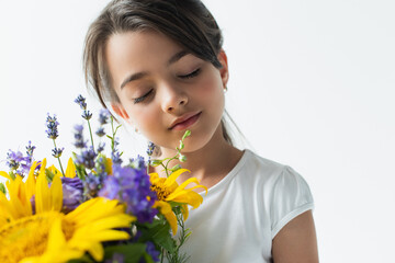 Portrait of kid closing eyes near blue and yellow flowers isolated on grey