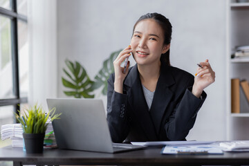 Portrait of young Asian smiling cheerful entrepreneur in casual office making a phone call while working with a laptop