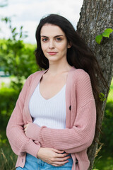 positive brunette woman standing with crossed arms in park and looking at camera