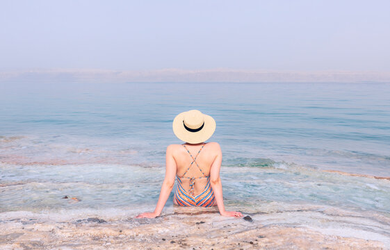 Attractive girl in swimsuit  with hat sitting on the shore of the dead sea
