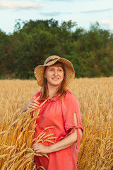 A woman in the evening among the wheat ears looks forward and smiles