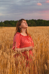 A woman in a wheat field looks at the sunset