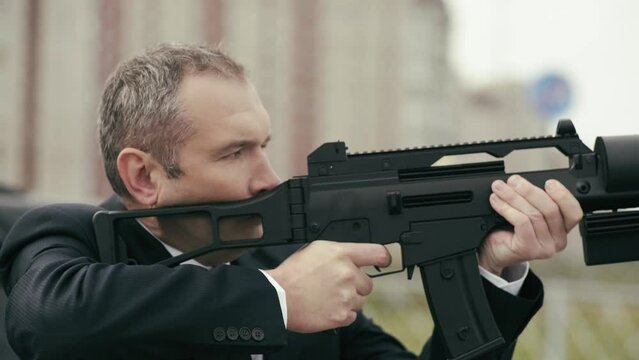 A man in a black suit aims a futuristic weapon.
