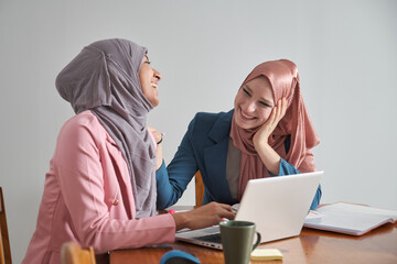 Two muslim business women wearing hijab laughing and working in a laptop. Businesswoman at work.