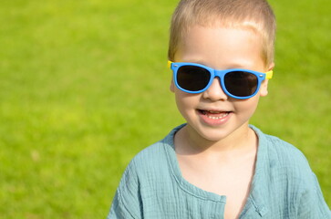 Portrait A five-year-old boy in black sunglasses against a green lawn. The child is sitting on the grass. Space for text. Summer concept: getting ready for school, a park for children, vacation