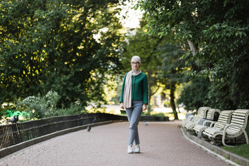 Full length portrait of beautiful smiling stylish muslim woman with in hijab walking in summer city park. Street style, summer, outdoor, break concept. Walking down the sunny park.