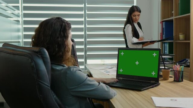 Woman side view working on laptop with chroma key screen. Female browsing internet on a green screen laptop in the office.