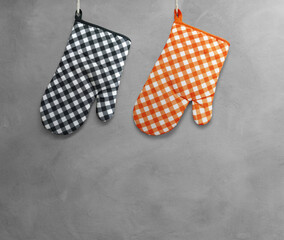 Orange and black heat resistant cooking gloves hanging on a cement wall.