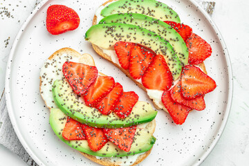 toasts or bruschetta with strawberry, avocado, soft cheese and chia seeds on a blue background....
