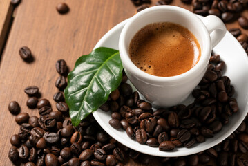 Tazzina di caffè espresso napoletano con chicchi di caffè tostato e foglia su tavolo in legno
