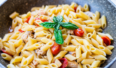 Italian pasta with swordfish, cherry tomatoes, oil and basil in a pan on a table Selective focus