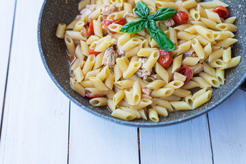 Italian pasta with swordfish, cherry tomatoes, oil and basil in a pan on a table Selective focue