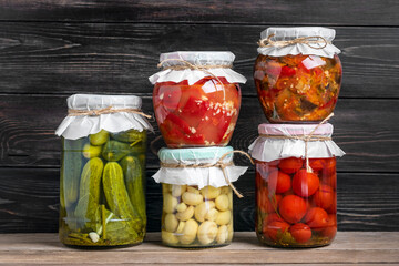 Homemade pickled cherry tomatoes, cucumbers, champignons, garlic, eggplant, red peppers in jars on wooden shelf Homemade canned and fermented foods concept Seasonal product