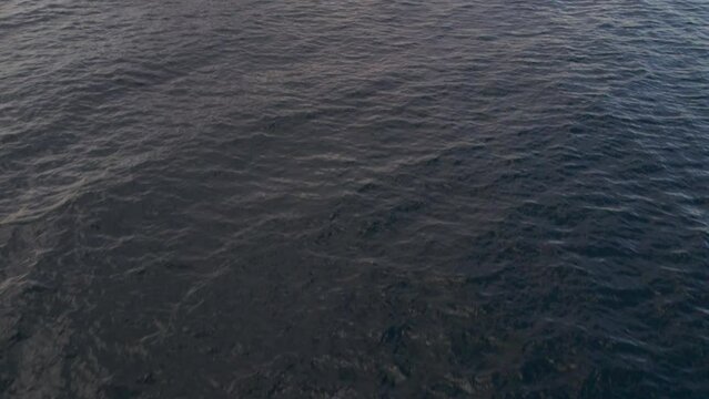 Aerial view of the wavy sea and the rocky mountains gleaming under the cloudy blue sky in 4K
