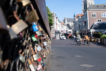 Obraz premium Cityscape small northern european city. Padlocks closed on river bridge, people cycling on street with small old houses and old cathedral tower. Breda, the Netherlands