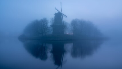 Windmill and trees on the lakeshore on a foggy day