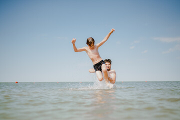 Dad swims with his son in the sea. The father throws his son in the water. The boy does a somersault in the sea. The family spends their summer vacation at the sea.