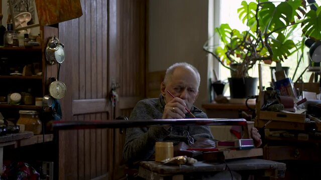 Elderly male master works in his workshop restoring japanese sword