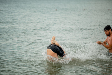 Dad swims with his son in the sea. The father throws his son in the water. The boy does a somersault in the sea. The family spends their summer vacation at the sea.