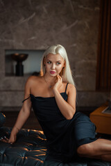 Naklejka premium portrait of a luxurious young blonde woman in a black sexy dress In a dark interior