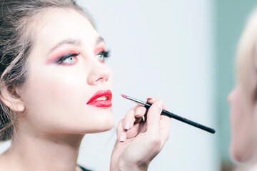 Makeup. Makeup artist applies red lipstick. Beautiful female face. Sensual lips. Close-up.