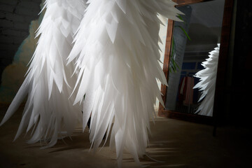 Angel wings with white feathers and their reflection in the mirror standing against the wall...