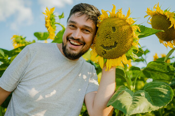 A man stands near a sunflower and smiles, rejoices at a good harvest. A young farmer stands in a...