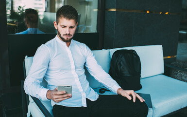 Serious man with smartphone on couch