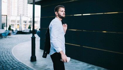 Fototapeta na wymiar Serious man with smartphone standing on street near modern building