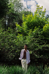 young african american man in summer clothes standing with hand in pocket in summer park