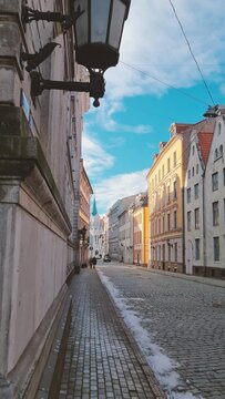 Vertical video. Walking walk through the streets of the old old town of Riga in the spring. Bright sun with long shadows on the paving stones. Medieval buildings and churches. Latvia