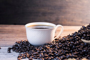 Black coffee in a white coffee cup with hot steam and coffee beans placed on a wooden table on a dark background. in a warm atmosphere