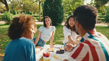 Happy smiling young multinational people at picnic on summer day outdoors. Friends have fun weekend together, relaxing in the park at picnic