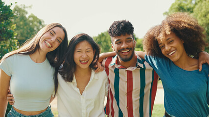 Happy multiethnic young people walk embracing on summer day outdoors. Group of friends are talking...