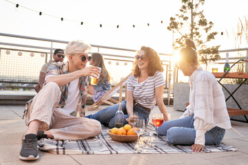 Group of caucasian friends sitting and talking together at the rooftop in summer day