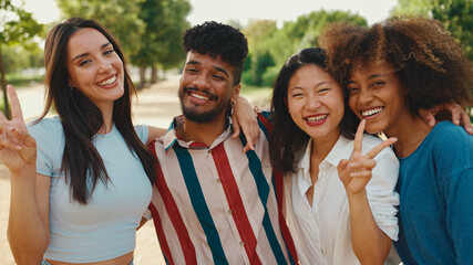 Happy, lovely multiethnic young people posing for the camera on summer day outdoors. group of friends hugging each other smiling at the camera while standing on path in the park
